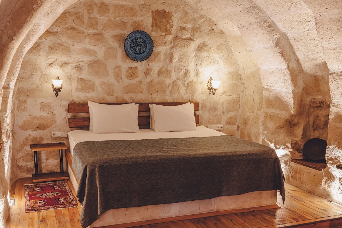 A rustic stone-walled bedroom with a wooden bed, two bedside tables, and a decorative plate on the wall.