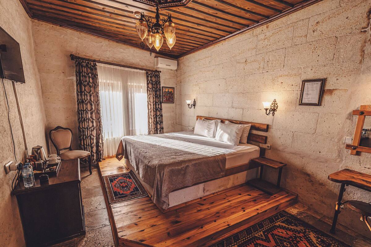 A bedroom with a wooden bed, a chair, a desk, a mirror, and a chandelier.