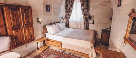 A room with a bed, wooden wardrobe, and a small table with a remote control.