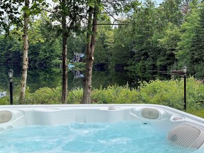 Un jacuzzi con vistas a un área boscosa y una casa al fondo.