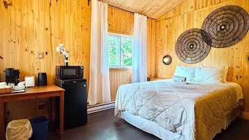 Una habitación de madera con una cama, un escritorio con una computadora y un microondas, una ventana con cortinas y un adorno en la pared.