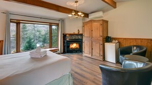 A room with a bed, a fireplace, wooden cabinets, and a view of trees through large windows. - Hôtel du Lac Lenore (Sainte-Adele)