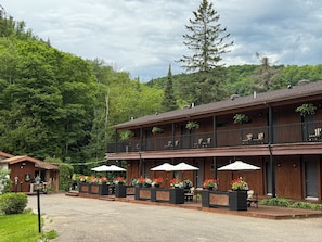 A two-story wooden building with outdoor seating and potted plants. - Hôtel du Lac Lenore (Sainte-Adele)