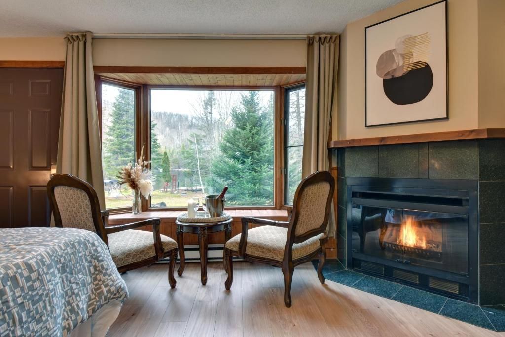 A room with a fireplace, a bed, a window with a view of trees, and a table with chairs.
