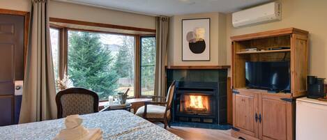 A hotel room with a bed, a fireplace, a television, and a view of the outdoors.