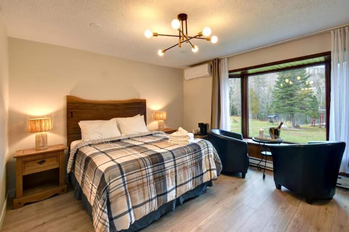 A bedroom with a large bed, two bedside tables, a desk, a chair, and a view of the outdoors.
