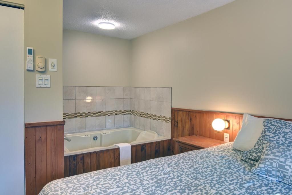 Un dormitorio con una cama grande, cabecera de madera, mesita de noche, lámpara de pared e hidromasaje integrado.