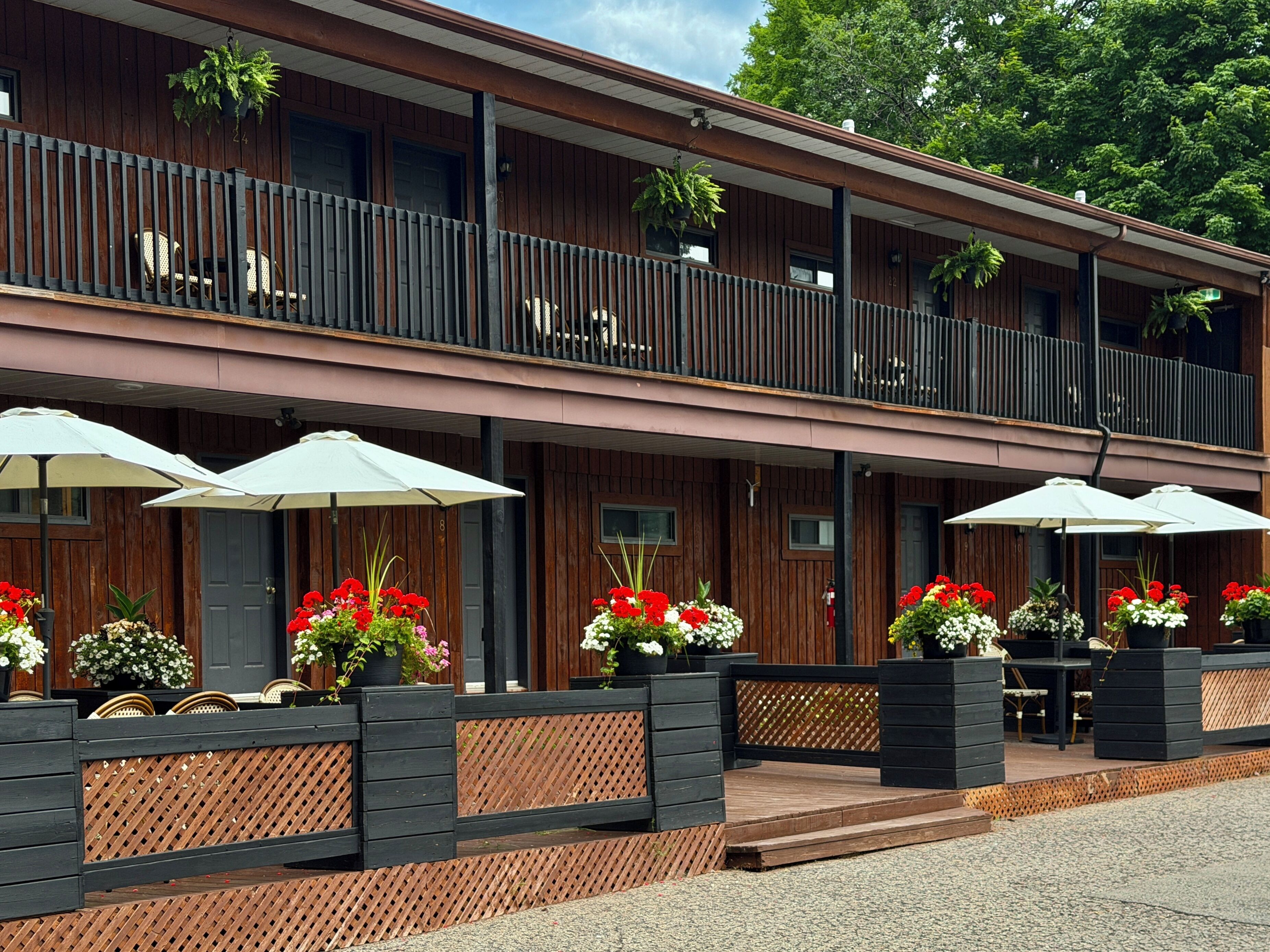 A two-story building with a balcony, outdoor seating with umbrellas, and potted plants.