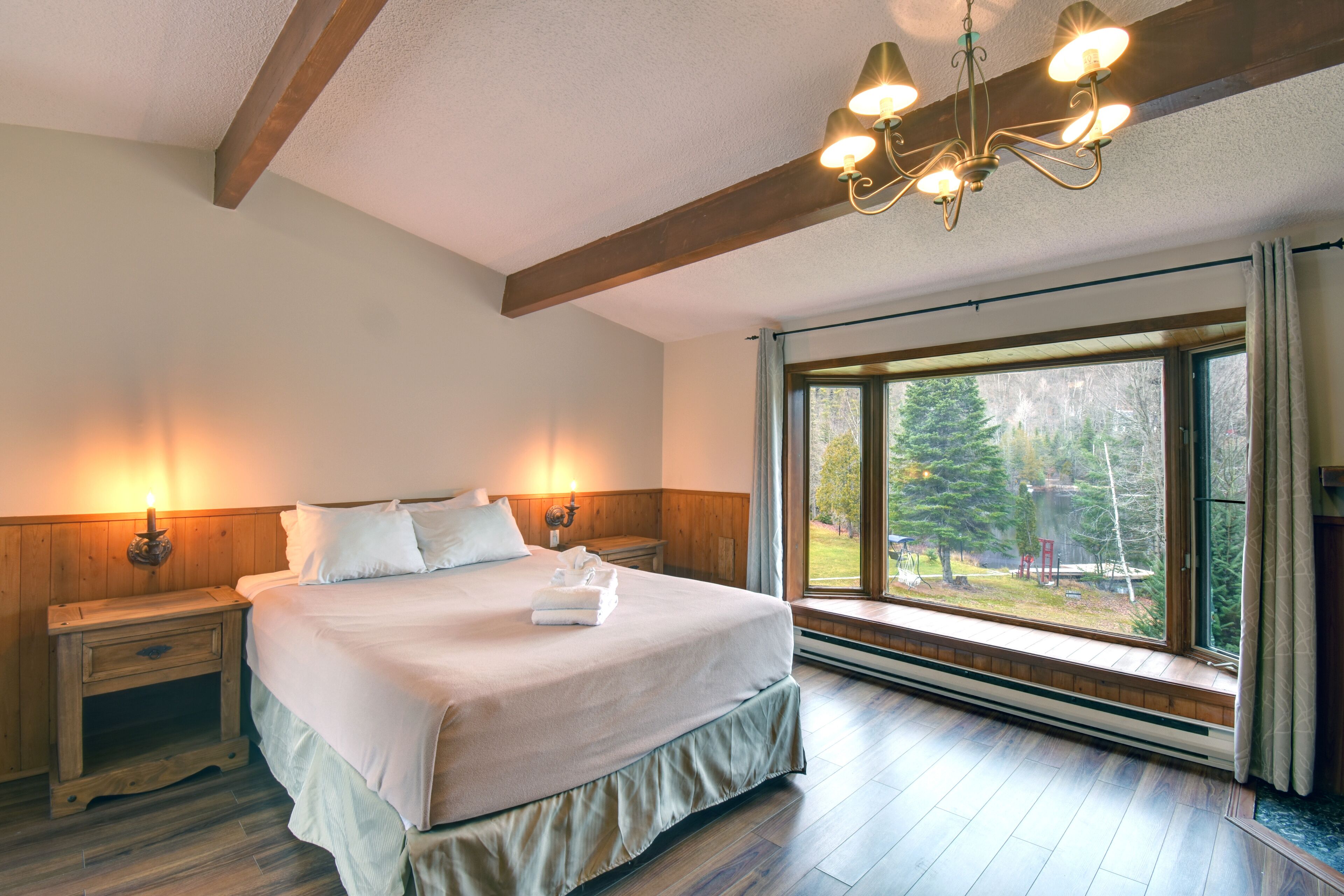 Un dormitorio con una cama grande, cabecera de madera, mesitas de noche y una ventana con vistas a árboles.