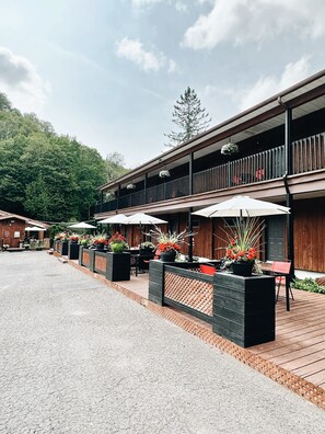 A wooden building with outdoor seating and potted plants. - Hôtel du Lac Lenore (Sainte-Adele)