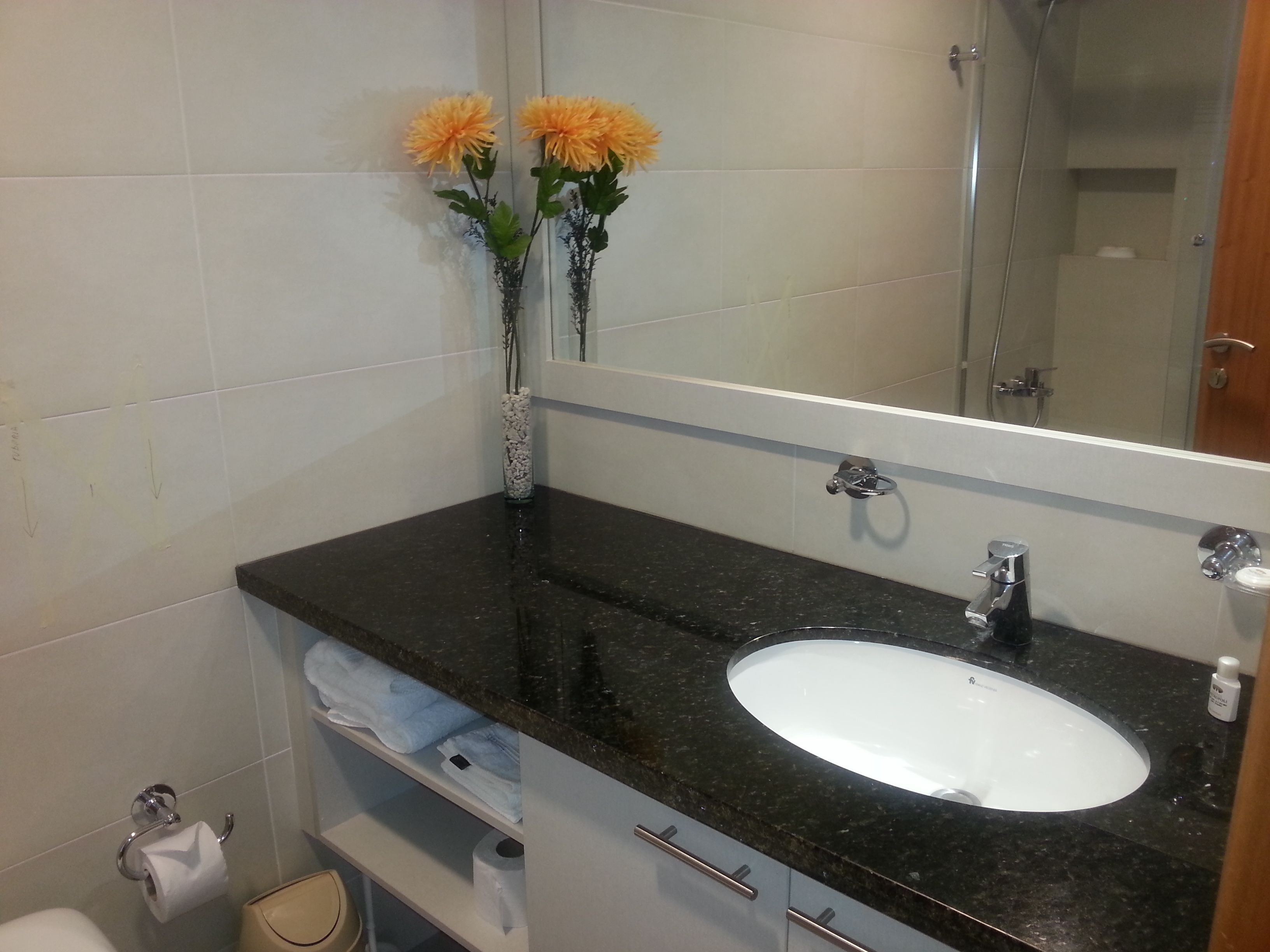 Une salle de bain avec un lavabo blanc, un plan de toilette foncé et deux vases ornés de fleurs.