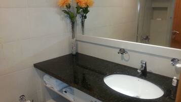 Une salle de bain avec un lavabo blanc, un plan de toilette foncé et deux vases ornés de fleurs.