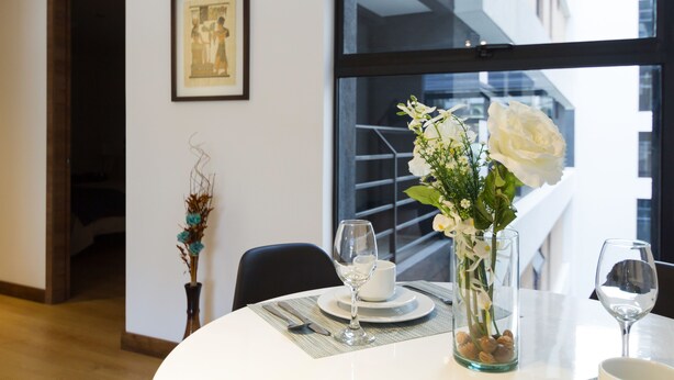 A dining area with a table set for two, featuring a vase with flowers and a framed picture on the wall. - Suites Metropoli Edificio Torino (Quito)