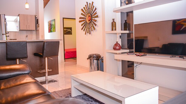 A modern living room with a sofa, a coffee table, a TV, and a kitchen area with a sink and cabinets. - Casa 14 (Medellín)