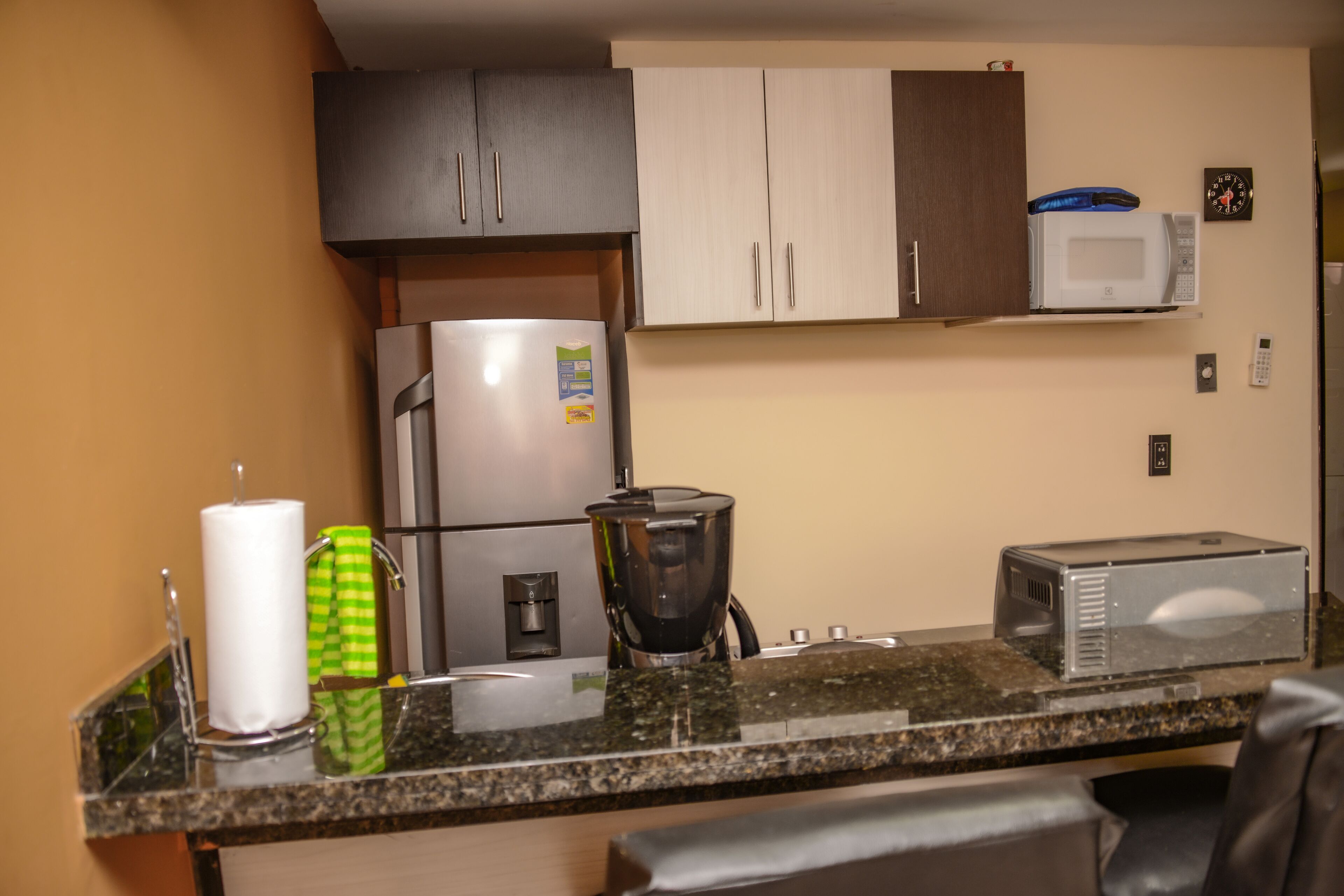A compact kitchen with a refrigerator, microwave, coffee maker, and a toaster on the countertop.