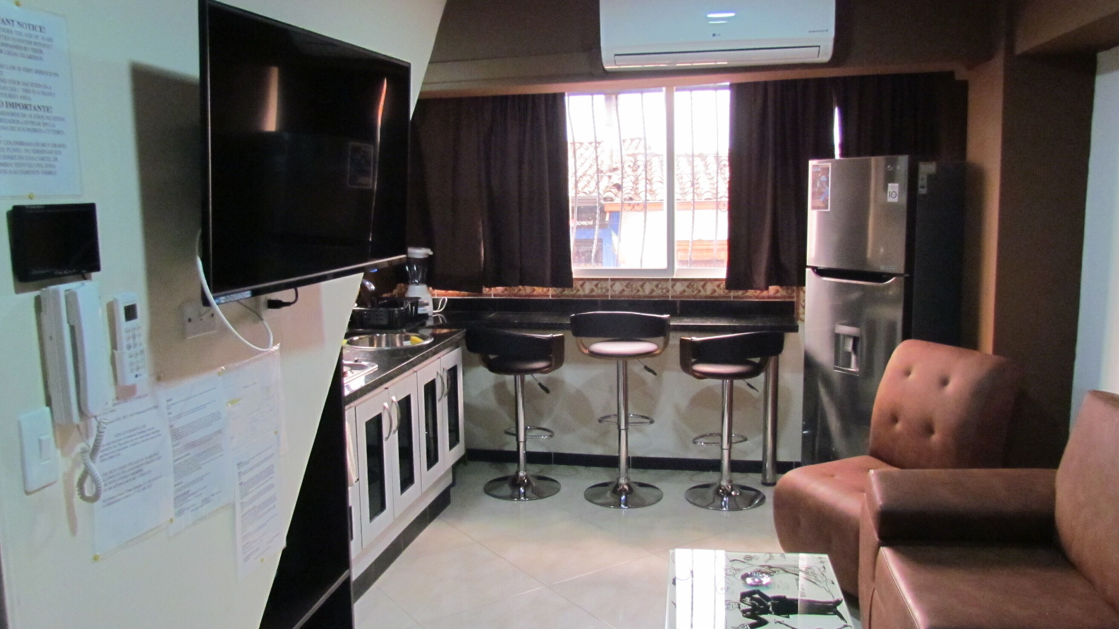 A compact kitchen with a TV, refrigerator, and bar stools.