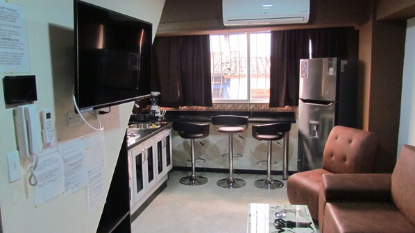 A compact kitchen with a TV, refrigerator, and bar stools.