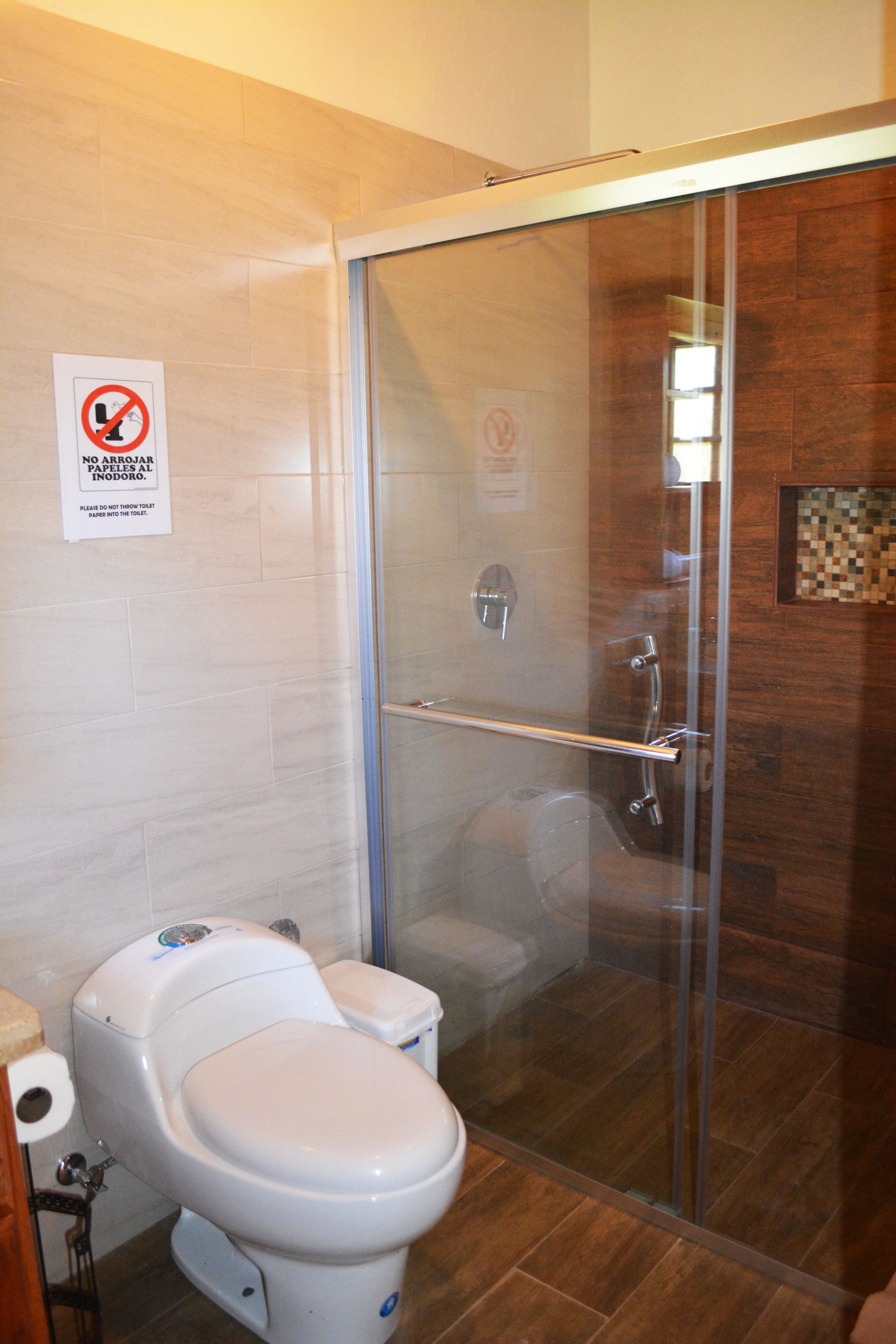 Une salle de bain avec une douche à parois de verre, des toilettes et un panneau indiquant qu’il est interdit de sécher les serviettes.