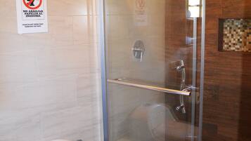 Une salle de bain avec une douche à parois de verre, des toilettes et un panneau indiquant qu’il est interdit de sécher les serviettes.