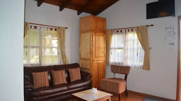 Un salón con un sofá de cuero marrón, un aparador de madera, un sillón a rayas y una pequeña mesa con un papel.