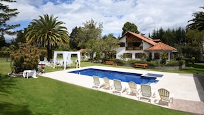 En swimmingpool med liggestole, en hvid pavillon og et hus med et tegltag.