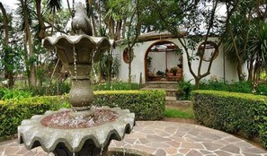 Una font de pedra en un jardí amb un edifici blanc al fons.
