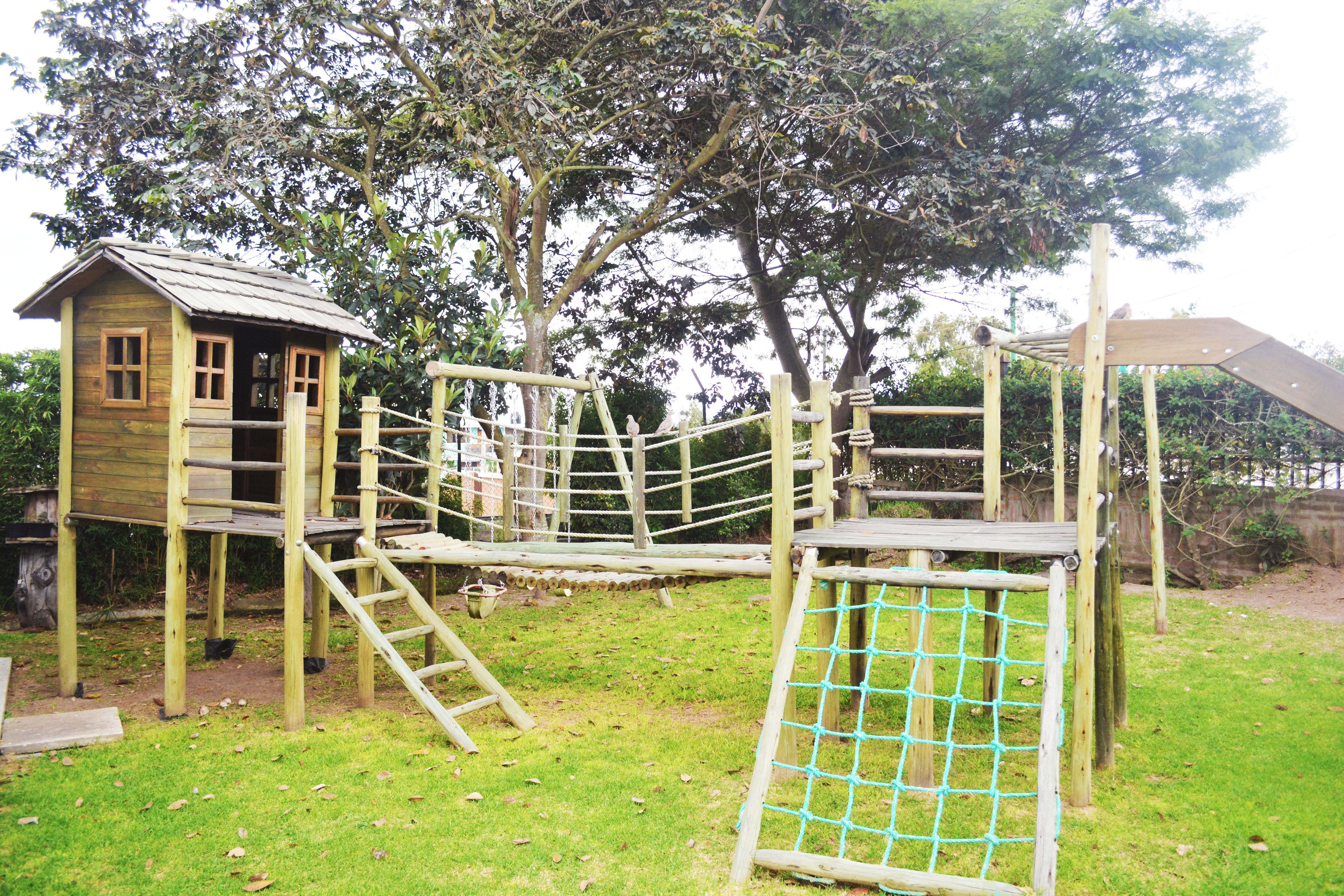 Una estructura de juego de madera con un puente de cuerda y una casita de madera.