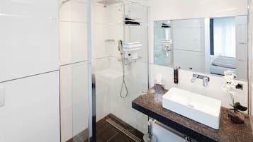 Un baño moderno con ducha de vidrio, un lavabo blanco y un espejo grande.