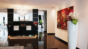 A modern reception area with a black counter, a chandelier, and a large floral painting on the wall. - Kurhaus Design Boutique Hotel (Erwitte)