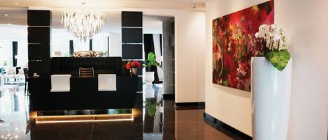 Un área de recepción moderna con un mostrador negro, una araña y un cuadro grande con motivos florales en la pared.