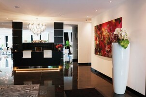 Uma área de recepção moderna com um balcão preto, um candelabro e um grande quadro com flores na parede.