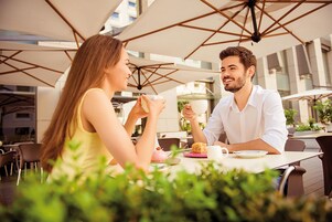 Um casal jantando em um café ao ar livre, com guarda-sóis e mesas.