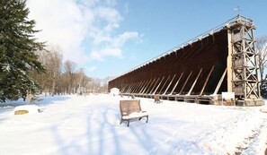 A snow-covered outdoor area with a wooden bench and a large wooden structure with a metal framework.