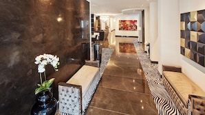 A modern hotel lobby with a marble floor, a reception desk, and a seating area with patterned cushions. - Kurhaus Design Boutique Hotel (Erwitte)