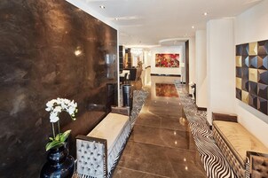 Um hall de hotel moderno, com piso de mármore, balcão de recepção e área de estar com almofadas estampadas.
