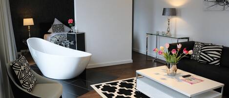 Un salon moderne avec une baignoire blanche, un canapé agrémenté de coussins à motifs, une table basse avec un magazine et un vase décoratif rempli de fleurs.