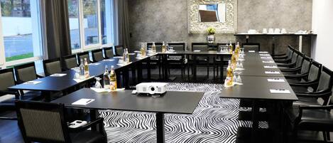 A conference room with a long table, chairs, a projector, and a patterned carpet.