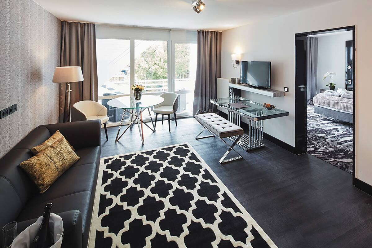 A hotel room with a sofa, a dining table, a TV, and a view of the outdoors.