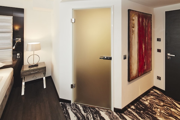 A hotel room with a bed, bedside table with a lamp, a door, and a large abstract painting on the wall. - Kurhaus Design Boutique Hotel (Erwitte)