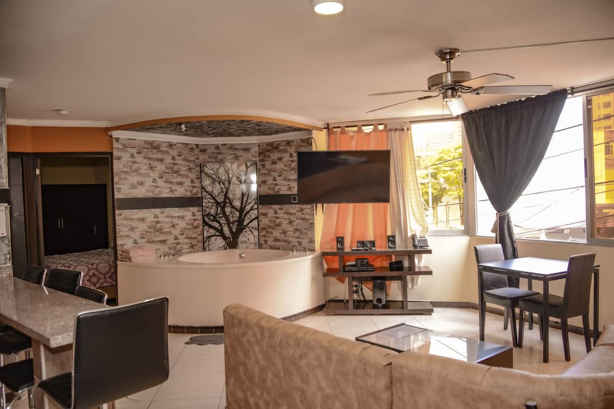 A modern living room with a large TV, a ceiling fan, a dining area, and a bathtub.