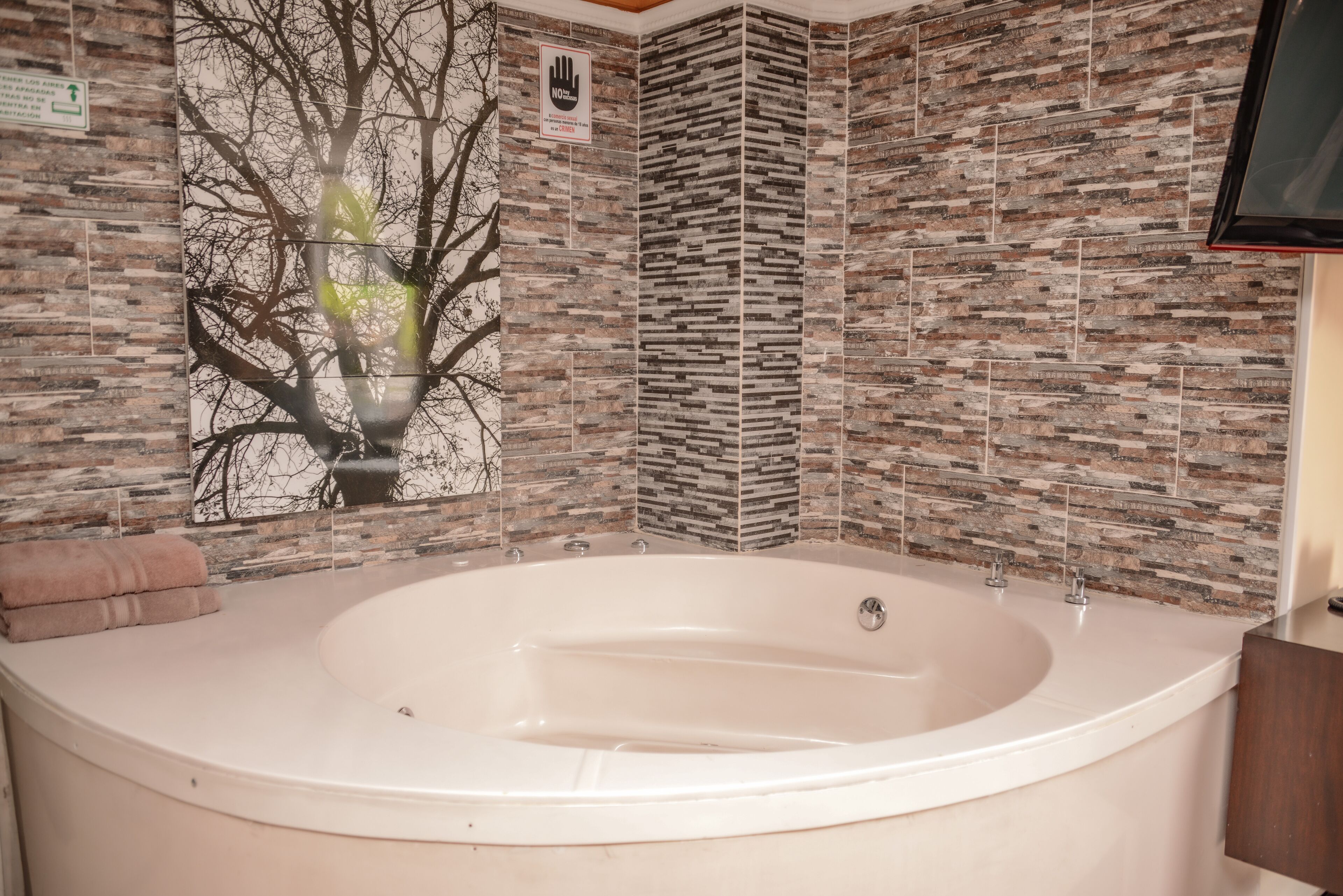 A bathroom with a large bathtub, a tree mural on the wall, and a tiled backsplash.