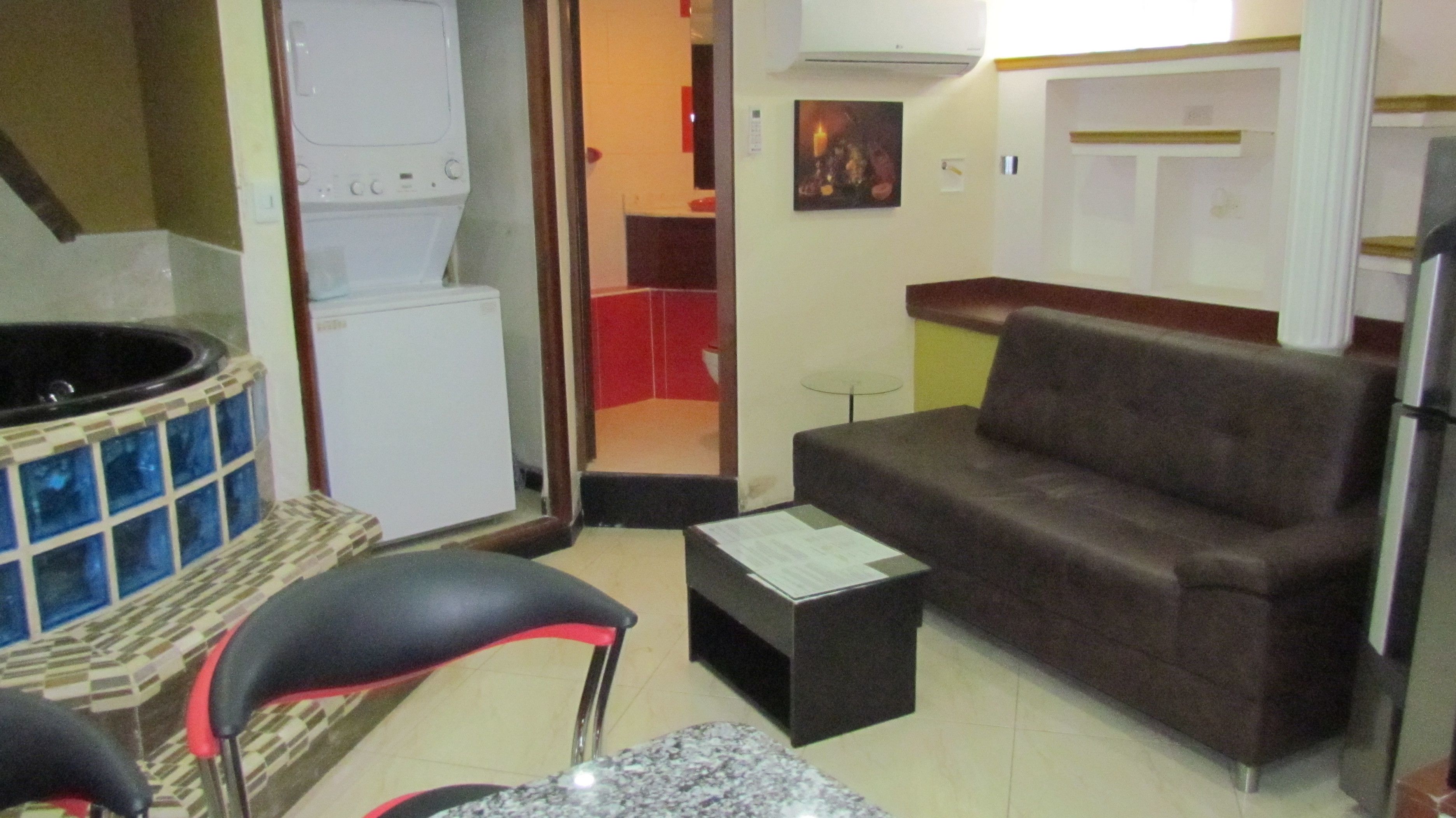 A compact living space with a sofa, a small table, a chair, a refrigerator, and a hot tub.