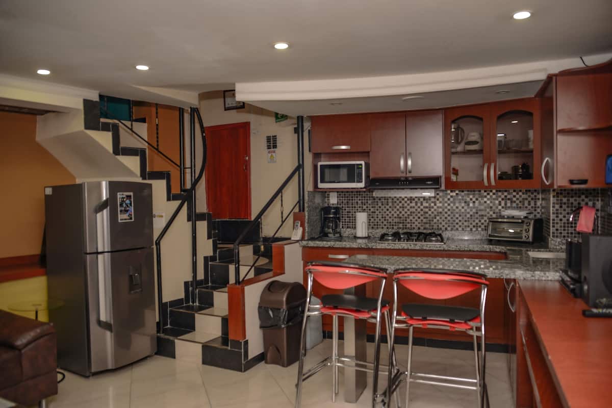 A kitchen with a refrigerator, microwave, toaster, and bar stools.