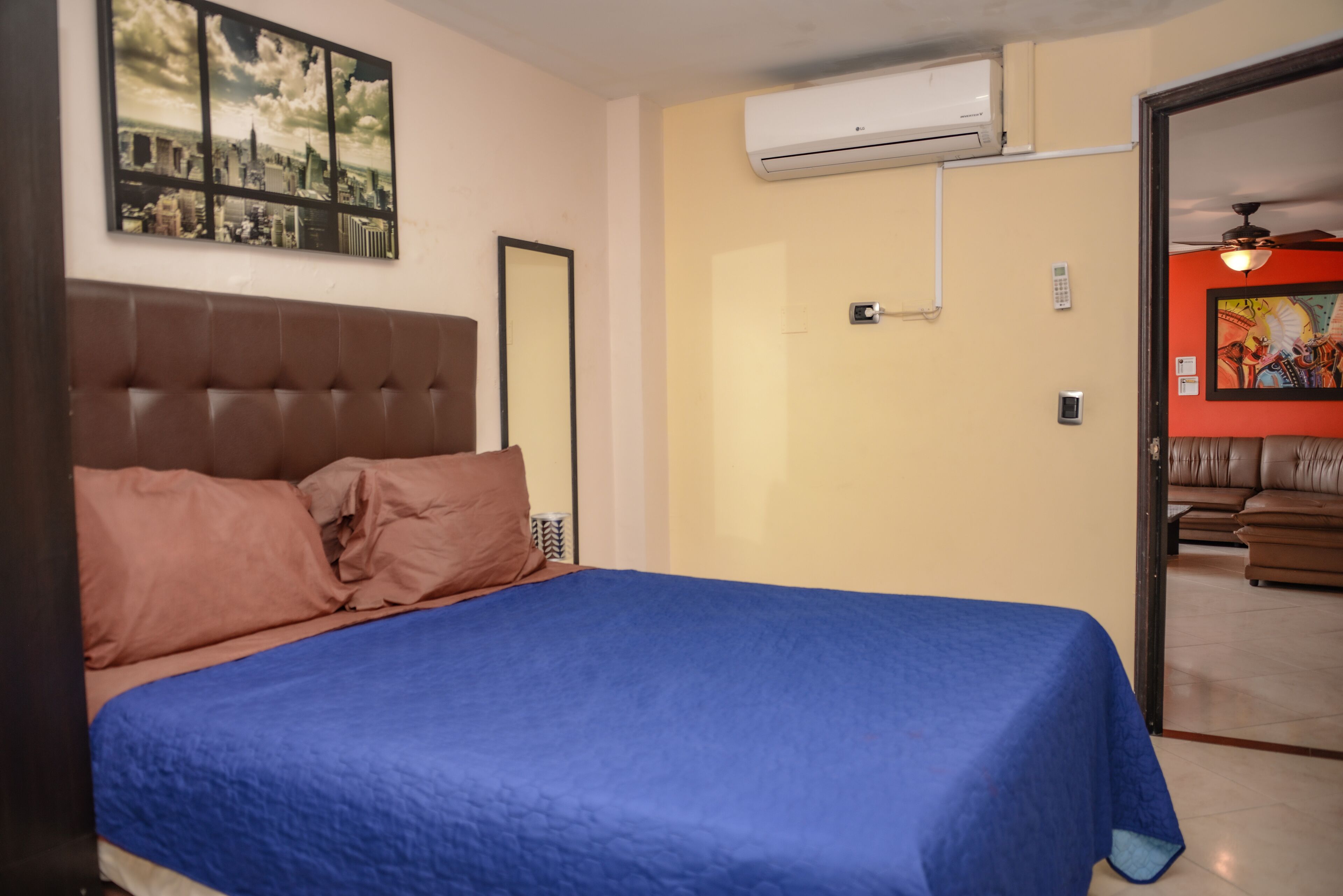 Een slaapkamer met een bed, een stadsgezicht schilderij, een airconditioning en een deur naar een andere kamer.