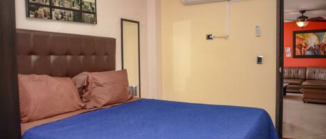 Een slaapkamer met een bed, een stadsgezicht schilderij, een airconditioning en een deur naar een andere kamer.