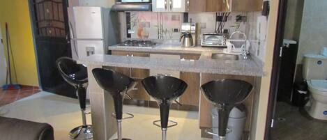 A modern kitchen with a central island, bar stools, a refrigerator, microwave, and various appliances.