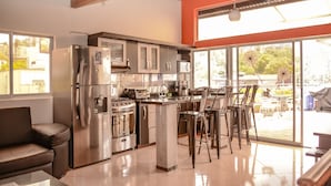 A modern kitchen with stainless steel appliances, a large island with bar stools, and large windows offering a view of the outdoors. - 10A Apartments (Medellín)