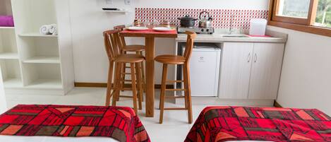 Una habitación de hotel pequeña con kitchenette, dos camas individuales, televisión y ventana con vistas.