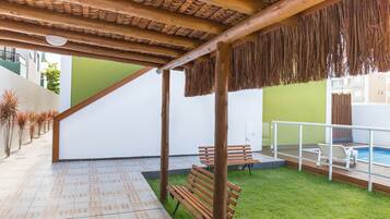 Uma área externa coberta com bancos de madeira, piscina e gramado.