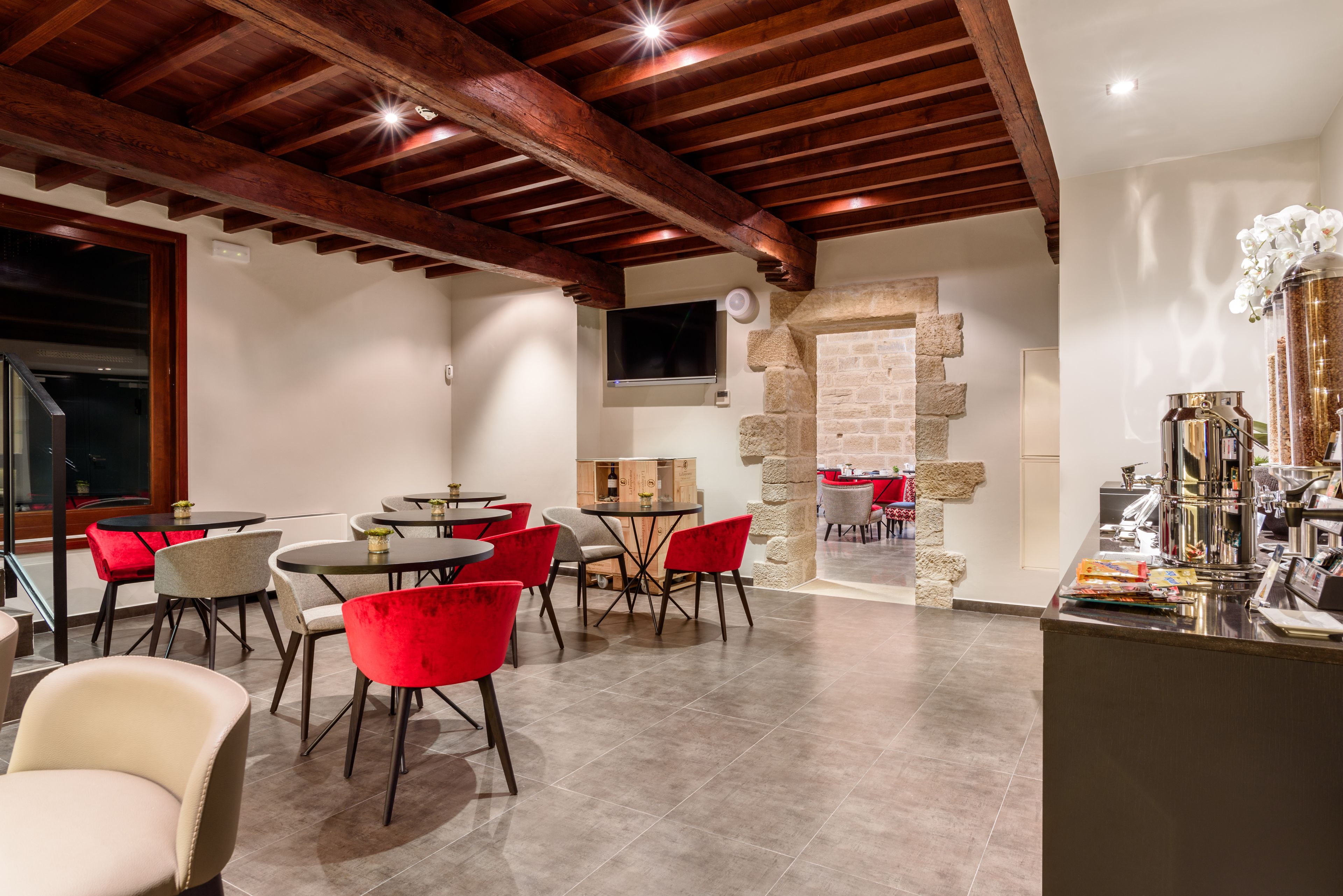 Un comedor con mesas y sillas redondas, un arco de piedra y un televisor montado en la pared.